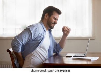 Unhappy Caucasian Man Sit At Desk In Home Office Work On Laptop Suffer From Lower Back Muscle Strain Or Spasm. Unwell Unhealthy Male Have Backache From Incorrect Posture. Sedentary Life Concept.