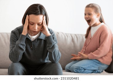 Unhappy caucasian middle aged mother suffers from screams and whims of daughter in living room interior. Relationship problems at home, parenting, scandal and stress with troubled teenager - Shutterstock ID 2311020481