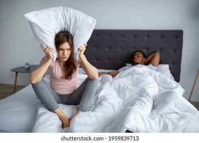 Unhappy Caucasian Woman Covering Ears With Pillow, Cannot Stand Loud Snore Of Her Husband, Sitting Angrily On Bed At Home, Copy Space. Young Lady Being Disturbed By Her Boyfriend's Snoring