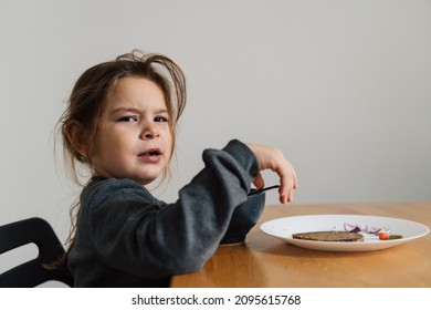 Unhappy Child Girl Eats Soup From Black Bowl With Bread And Onion. Lifestyle Photo Of Kid In Kitchen Having A Meal, Screaming Kid. Picky Eater