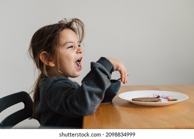 Unhappy Child Girl Eats Soup From Black Bowl With Bread And Onion. Lifestyle Photo Of Kid In Kitchen Having A Meal, Screaming Kid. Picky Eater