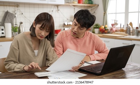 unhappy Chinese married couple calculating budget on calculator in dining room at home. the surprised man holding his head worrying about lack of money to pay the loan - Shutterstock ID 2136478947