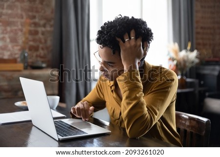 Unhappy confused millennial African American woman in glasses looking at laptop screen, stuck with difficult task or feeling stressed working with electronic documents, reading email with bad news.
