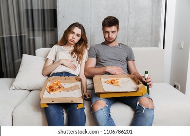 Unhappy Couple Ate Too Much Pizza While Sitting Together On A Couch At Home