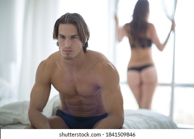 Unhappy Couple In The Bedroom. Man Sitting On Bed In Foreground Away From Woman. Sexual Issues, Erectile And Sex Dysfunction. 