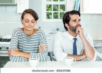 Unhappy Couple With Coffee Cup Sitting At Table In Kitchen