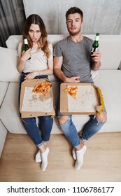 Unhappy Couple Eating Pizza While Sitting Together On A Couch At Home