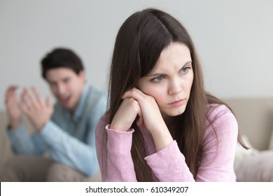 Unhappy couple having a dispute, sitting apart at home. Man shouting at woman and gesturing. Angry upset lady sitting her back to boyfriend and ignoring, not talking to guy. Troubles in relationships 