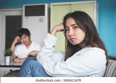 Unhappy Couple Not Talking After An Argument At Home. Depressed Woman Sitting On The Sofa And Sad Man Sitting On The Table Looking At Girlfriend. Selective Focus On Woman Face.