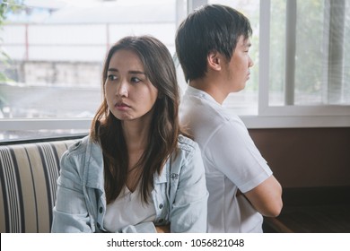 Unhappy Couple Not Talking After An Argument At Home. Depressed Woman Sitting On The Sofa And Sad Man Sitting On The Table Looking At Girlfriend. Selective Focus On Woman Face.