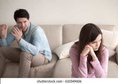 Unhappy couple quarrelling, sitting apart indoors. Aggressive guy is blaming woman, shouting at her. Annoyed girl ignoring man, not talking to boyfriend. Family problems concept, teenagers conflict 