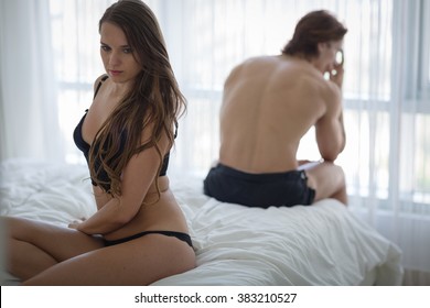 Unhappy couple sitting in bed away from each other. Woman in foreground. 