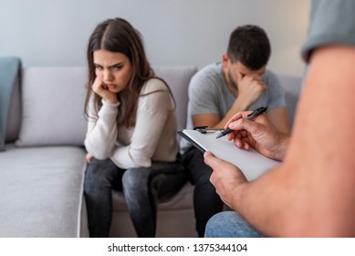 Unhappy couple at therapy session with man talking to therapist in therapists office. Sad couple listening to a marriage counselor during a therapy sitting on a sofa at home - Powered by Shutterstock