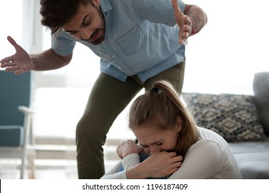 Unhappy Crying Frightened Woman And Aggressive Man Quarrelling At Home. Angry Husband Emotionally Arguing Screaming Shouting To Scared Wife Psychological Emotional Abuse And Domestic Violence Concept