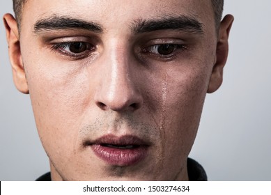 Unhappy crying young man with dropping tears on the face. Closeup studio portrait on grey background. Negative emotional concept. Toned contrast color