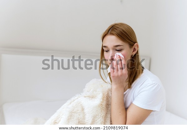 Unhappy depressed caucasian\
woman crying and wiping away her tears with a paper napkin,\
suffering from grief in the family. The woman is crying at home in\
her bed