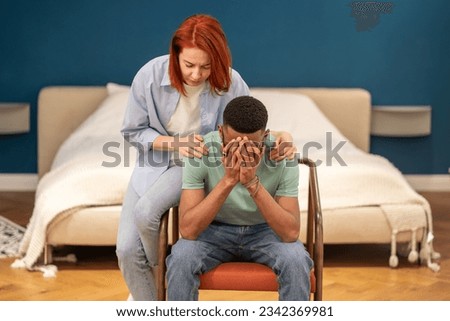 Unhappy diverse couple discussing divorce at home, husband feeling sad and frustrated after difficult conversation with wife. Loving girlfriend trying to comfort crying boyfriend embracing him