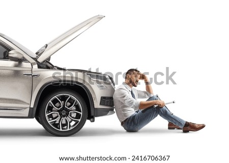 Unhappy driver sitting on the ground in front of a SUV with open hood isolated on white background