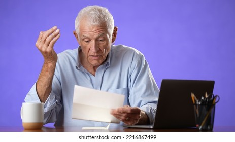 Unhappy Elderly Old Man Sitting At Desk Using Laptop Computer Tired And Getting Bad News, Bills To Pay, No Money Isolated On Solid Purple Background