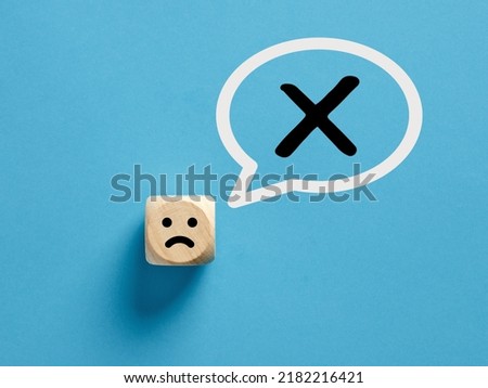 Unhappy face icon on a wooden cube with cross x or no sign in a speech bubble. No or rejection concept.