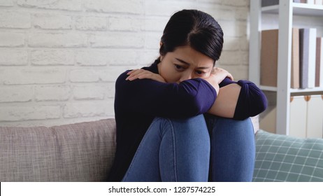 Unhappy female sit on sofa feeling lonely and sad. upset asian girl crying at home having relationships life problems. hurt young woman on couch coping with emotions after breakup bad news. - Shutterstock ID 1287574225