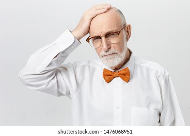 Unhappy Frustrated Caucasian Male Pensioner With Thick Beard Suffering From Memory Loss Problem Posing In Studio, Rubbing His Bald Head, Having Depressed Stressed Facial Expression, Frowning