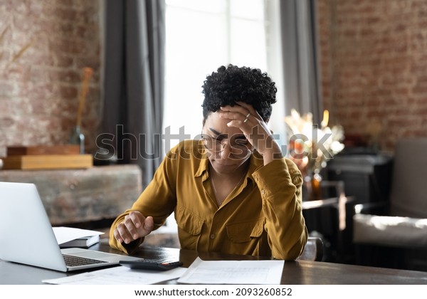 Unhappy frustrated young African American woman\
feeling stressed managing financial affairs or mistakes, suffering\
from lack of money calculating business expenditures, accounting,\
bankruptcy concept.