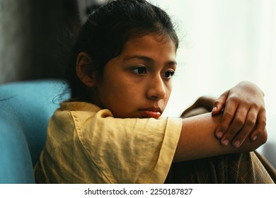 Unhappy girl portrait, Sad child sitting on sofa at home, Upset girl hugging knees alone, Concept of lonely girl and kid with trouble and violence - Powered by Shutterstock