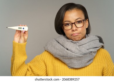 Unhappy Ill Female In Warm Scarf Showing Thermometer And Suffering From Fever. Upset African American Woman On Sick Leave Feel Bad And Unhealthy. Seasonal Flu Illness Or Coronavirus Treatment Concept