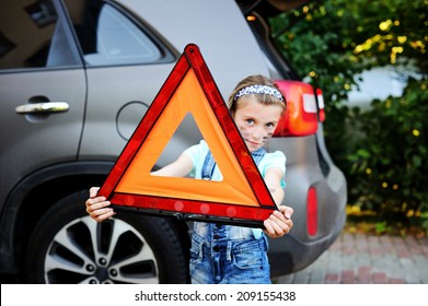 Unhappy Kid Girl Holds Red Warning Triangle On The Family Car Background