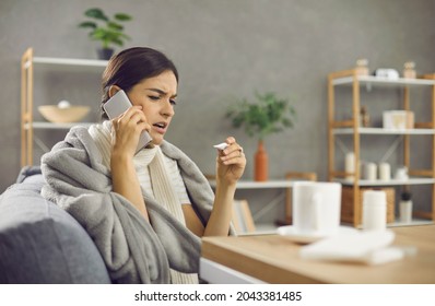 Unhappy lady who's having flu or cold fever calling in a doctor. Sick woman wrapped in warm blanket or plaid sitting on sofa at home, looking at thermometer in hand and making phone call to physician