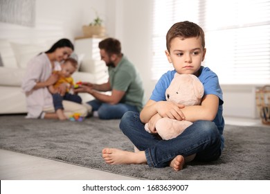 Unhappy little boy feeling jealous while parents spending time with his baby brother at home