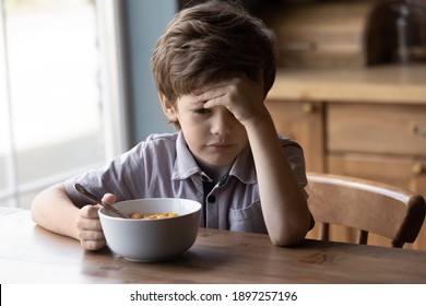 Unhappy Little Caucasian Boy Child Sit At Table At Home Kitchen Have No Appetite For Tasty Healthy Breakfast. Upset Stressed Small Kid Refuse To Eat Delicious Organic Cereals With Milk. Diet Concept.