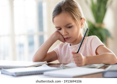 Unhappy Little Caucasian Girl Child Sit At Table At Home Feel Lazy Unmotivated Doing Homework Assignment. Upset Distressed Small 7s Kid Prepare School Task, Learn Study With Books. Education Concept.