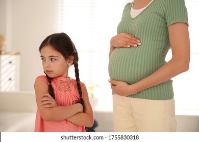 Unhappy little girl near pregnant mother at home. Feeling jealous towards unborn sibling