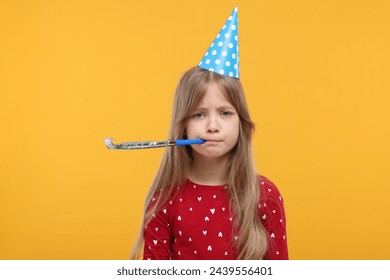 Unhappy little girl in party hat with blower on yellow background - Powered by Shutterstock