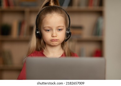 Unhappy Little Schoolgirl Video Calling Via Laptop Wearing Headset Learning Online Sitting At Home. Sad Kid Doing Homework Having Remote Class. Internet Education. Selective Focus