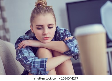 Unhappy lonely depressed teenage girl at home, she is sitting on the couch and propped her head with his feet. Depression of adolescence concept.