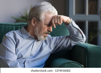 Unhappy Lonely Grey Haired Mature Man Sitting On Couch Alone, Holding Head On Hand, Sad Old Husband Missing Wife, Upset Middle Aged Male Lost In Thoughts, Elderly And Loneliness Concept Close Up