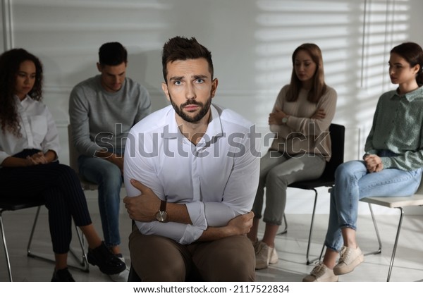Unhappy man and group of people behind his back\
indoors. Therapy\
session