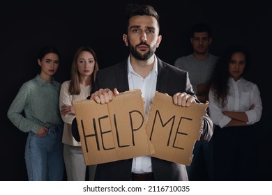 Unhappy Man With HELP ME Sign And Group Of People Behind His Back On Dark Background