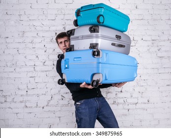 Unhappy man holding three heavy suitcases in hand. Travel light.