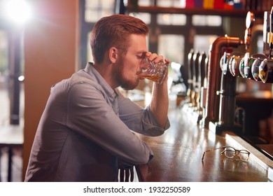 Unhappy Man Sitting At Pub Bar Drinking Alone With Glass Of Whisky