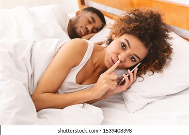 Unhappy marriage. Cheating black woman talking privately on cellphone, hiding from her sleeping husband