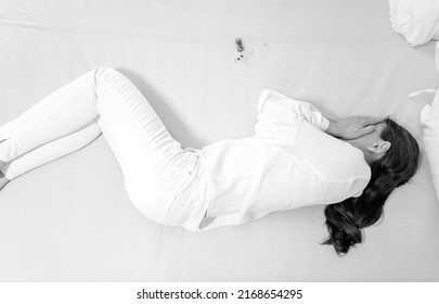 Unhappy Mature Lady Wearing Business Wear Lying On Her Bed With Bottle Of Pills. Sleeping Pills On Her Bed, Depressed Mature Woman Taking Medicine On Bed Before Sleeping.