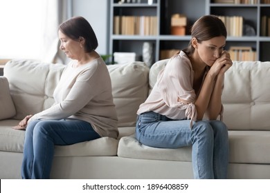 Unhappy Mature Mother And Grownup Daughter Ignoring Each Other After Quarrel, Sitting On Couch At Home Separately Back To Back, Avoiding Talking, Two Generations Of Women Conflict Concept