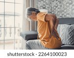Unhappy mature woman touching back, feeling pain, sitting on couch in living room, unhealthy middle aged senior female suffering from backache, spinal problem, rubbing stiff muscles or kidney