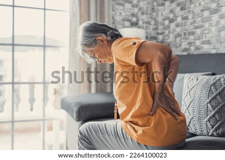 Unhappy mature woman touching back, feeling pain, sitting on couch in living room, unhealthy middle aged senior female suffering from backache, spinal problem, rubbing stiff muscles or kidney