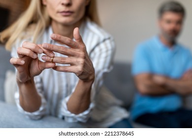 Unhappy middle aged european lady takes off ring, ignoring man during quarrel in living room interior, cropped. Relationship problems, divorce, scandal and breakup, emotions at home due covid-19