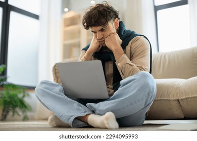 Unhappy Middle Eastern Man Using Laptop Computer Having Problem With Distance Work Sitting On Floor At Home. Freelancer Guy Reading Bad News Online. Freelance Career Issues Concept
